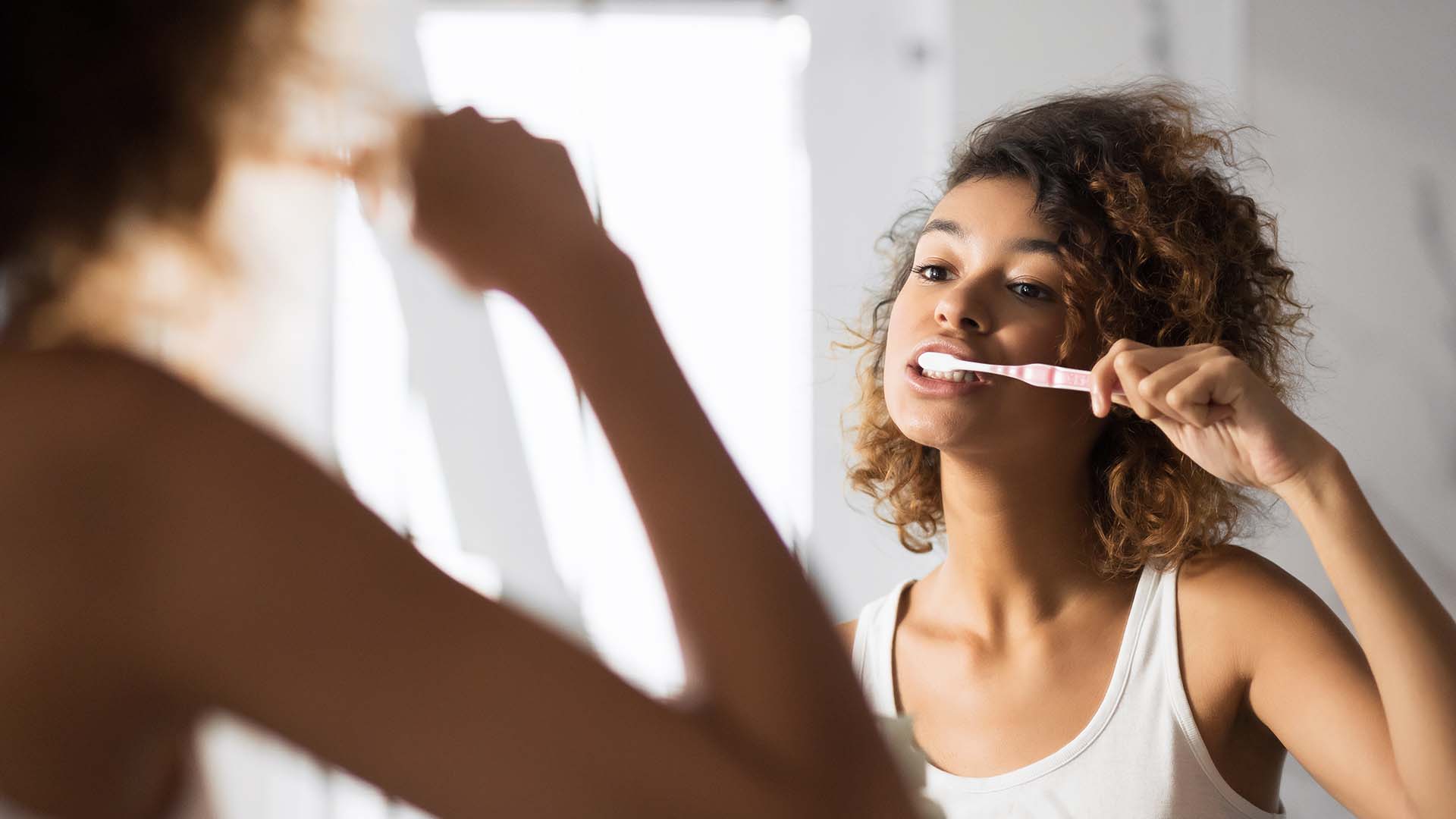 girl looks in mirror and brushes her teeth