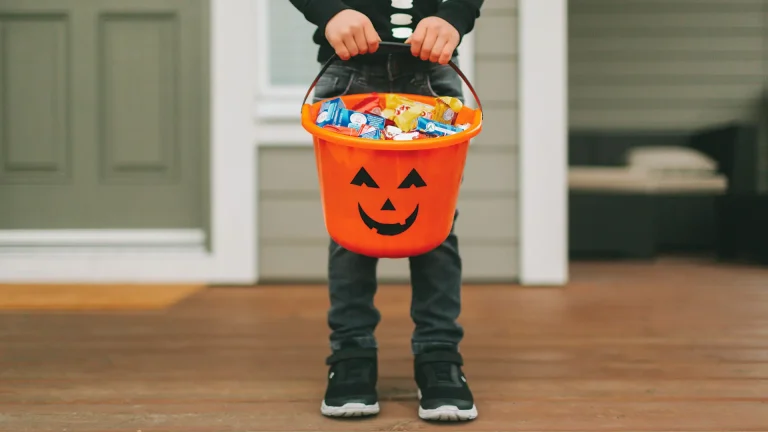 kid holding Halloween bucket full of candy