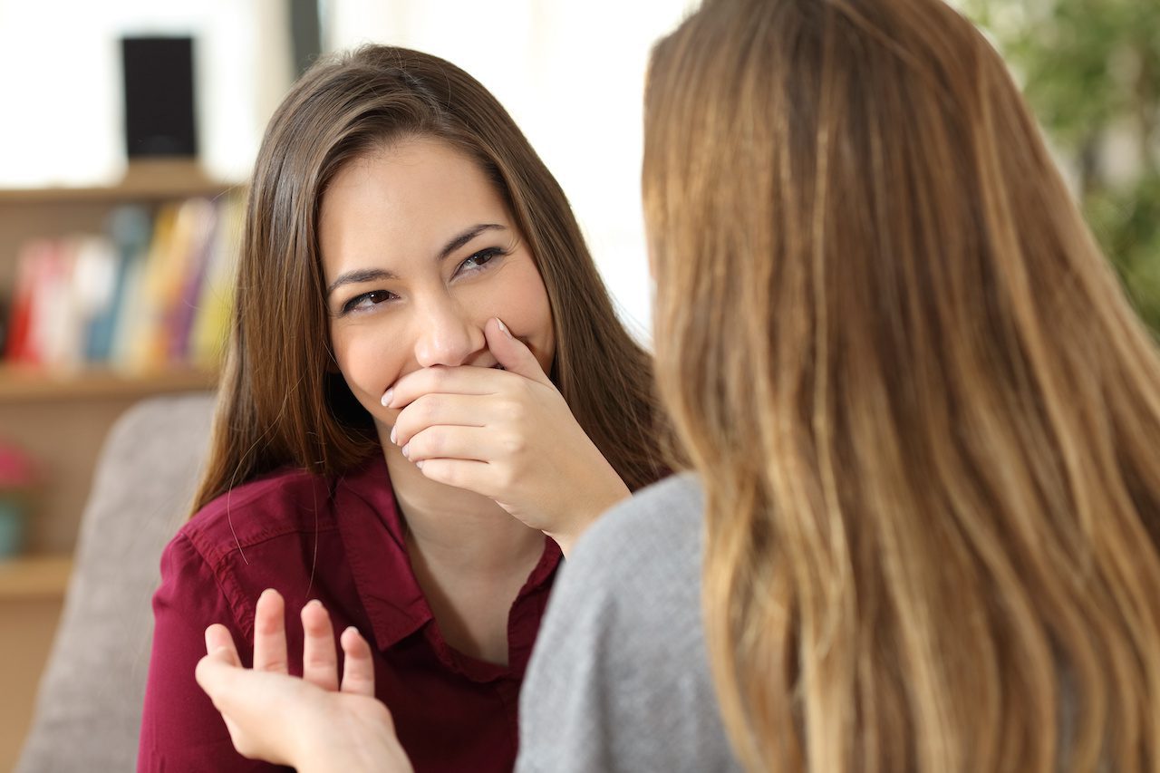 Ashamed woman hiding her smile in a conversation