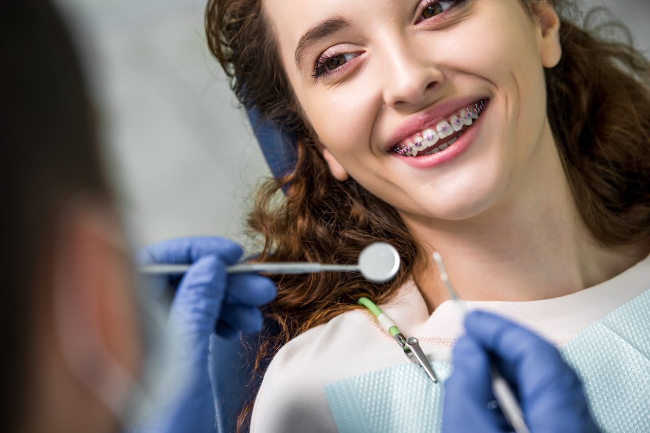 cheerful woman in braces during examination of teeth near dentist