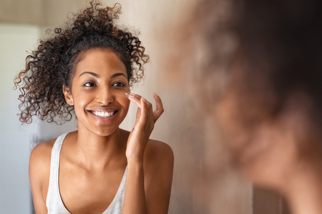women looking in mirror putting cream on her face